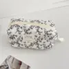 Trousse matelassée noire à motif fleuri rangée dans une valise, illustrant sa compatibilité voyage