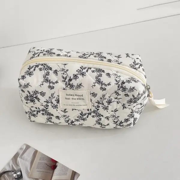 Trousse matelassée noire à motif fleuri rangée dans une valise, illustrant sa compatibilité voyage