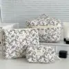 Trousse de toilette matelassée élégante avec motif floral noir sur fond capitonné, fermeture éclair dorée