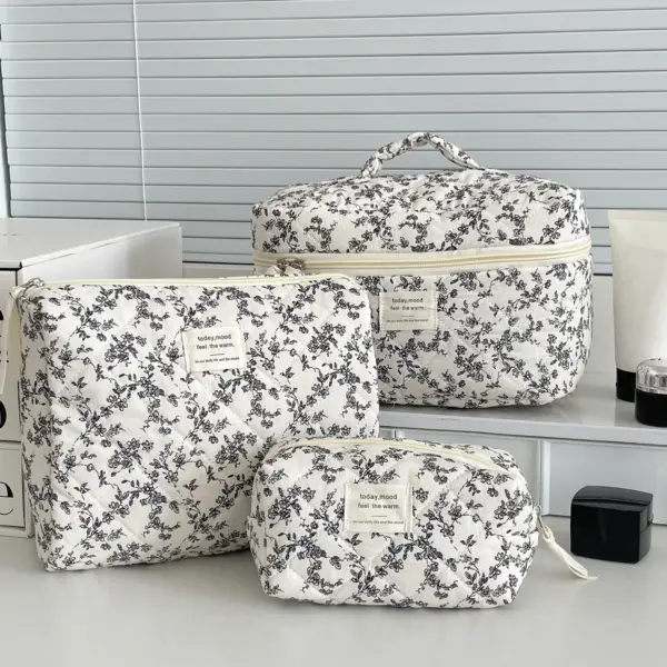 Trousse de toilette matelassée élégante avec motif floral noir sur fond capitonné, fermeture éclair dorée