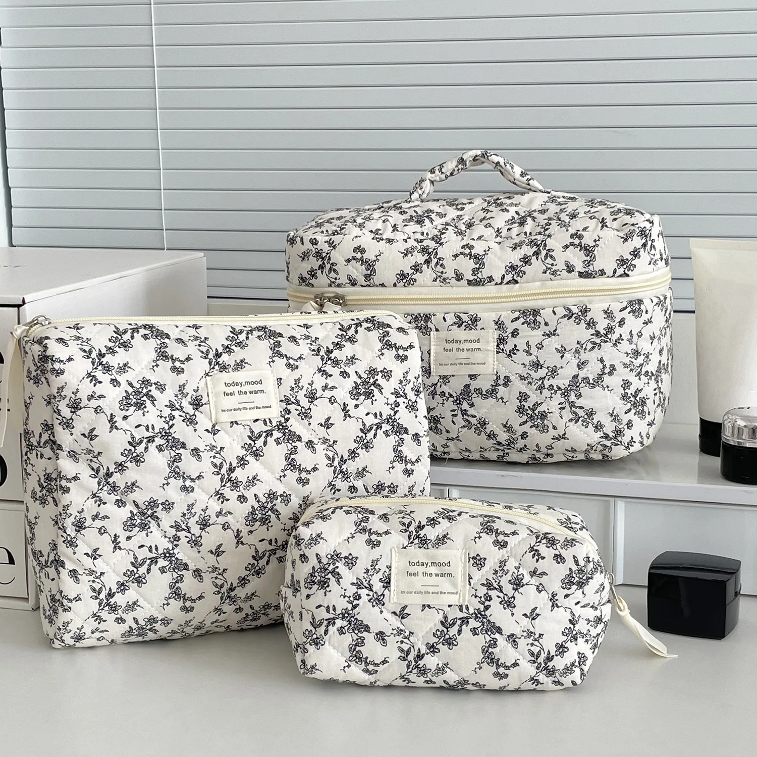 Trousse de toilette matelassée élégante avec motif floral noir sur fond capitonné, fermeture éclair dorée